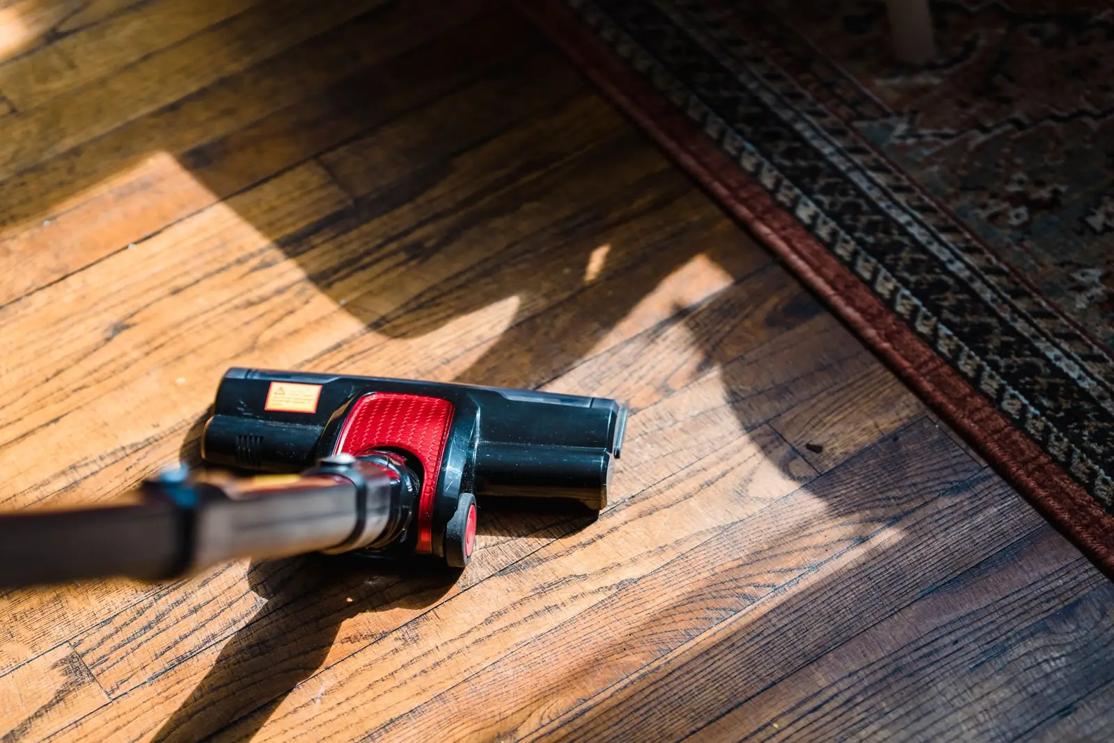 Cabezal de aspiradora, un electrodoméstico de casa, negro y rojo sobre un suelo de madera junto a una alfombra