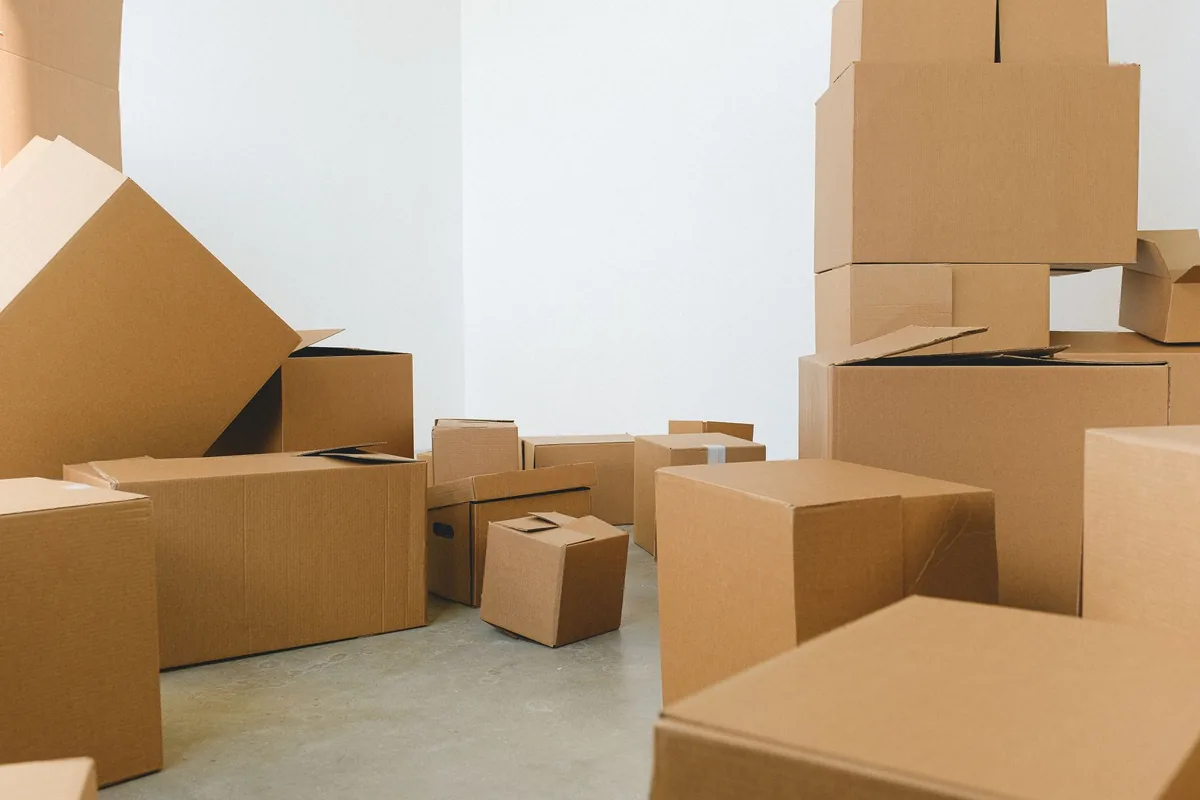 Montón de cajas de cartón de distintos tamaños, abiertas y cerradas, en una habitación vacía de paredes blancas