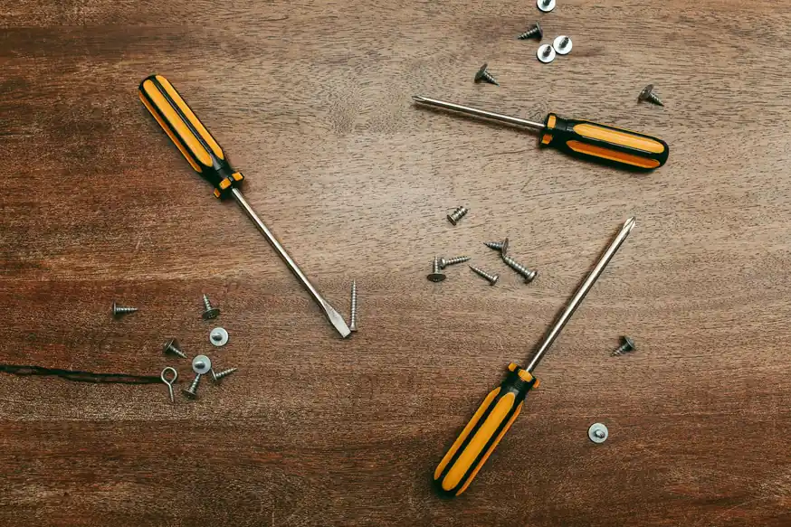 Tres destornilladores y varios tornillos sobre una mesa de madera