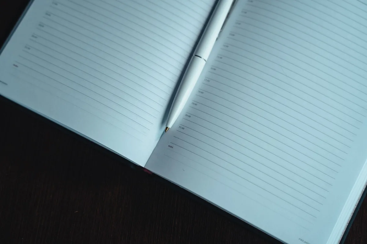 Cuaderno de agenda abierto con las horas impresas en cada línea y un bolígrafo blanco sobre la página