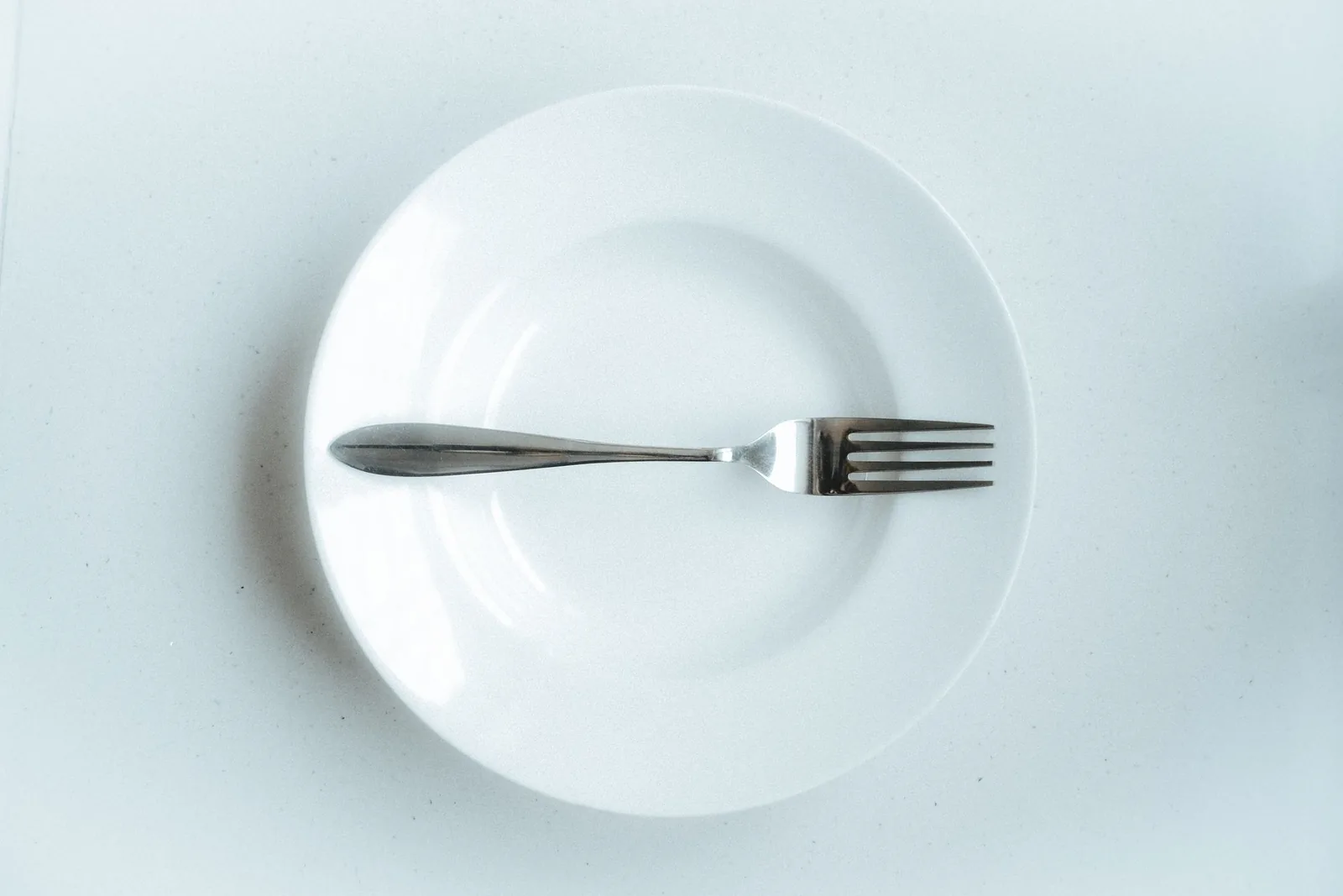 Plato blanco con un tenedor sobre una mesa blanca, un servicio de mesa para una sola persona