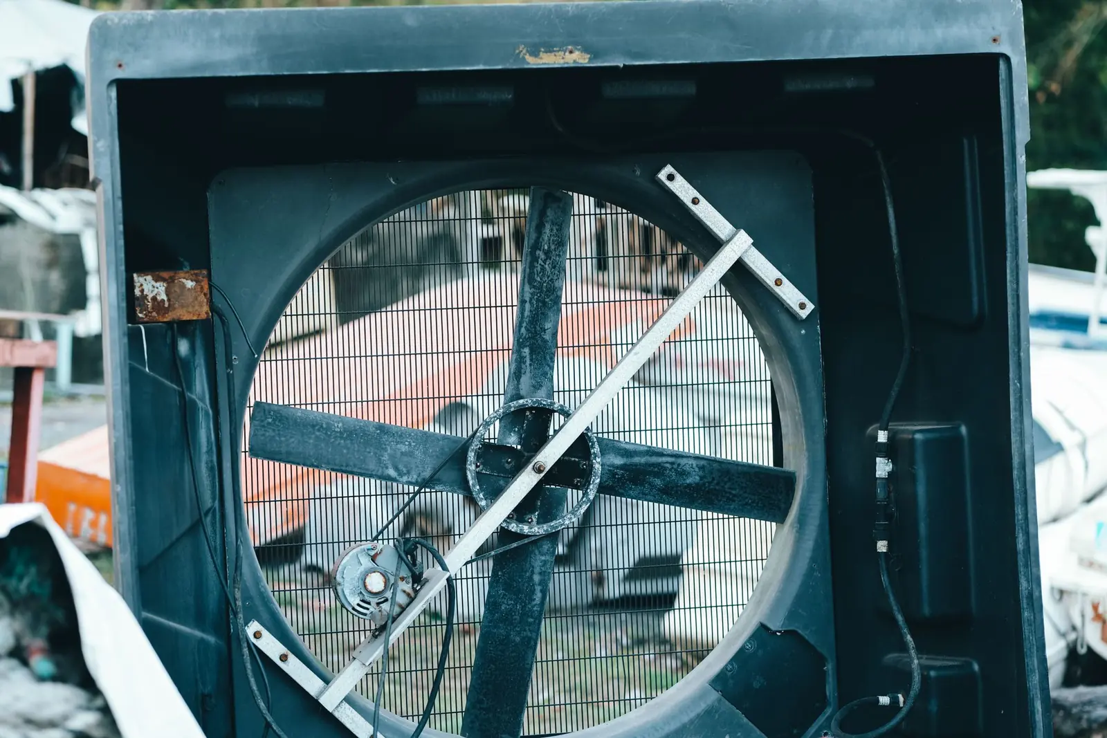 Ventilador grande de carcasa negra con las aspas y el motor a la vista, apartado al aire libre