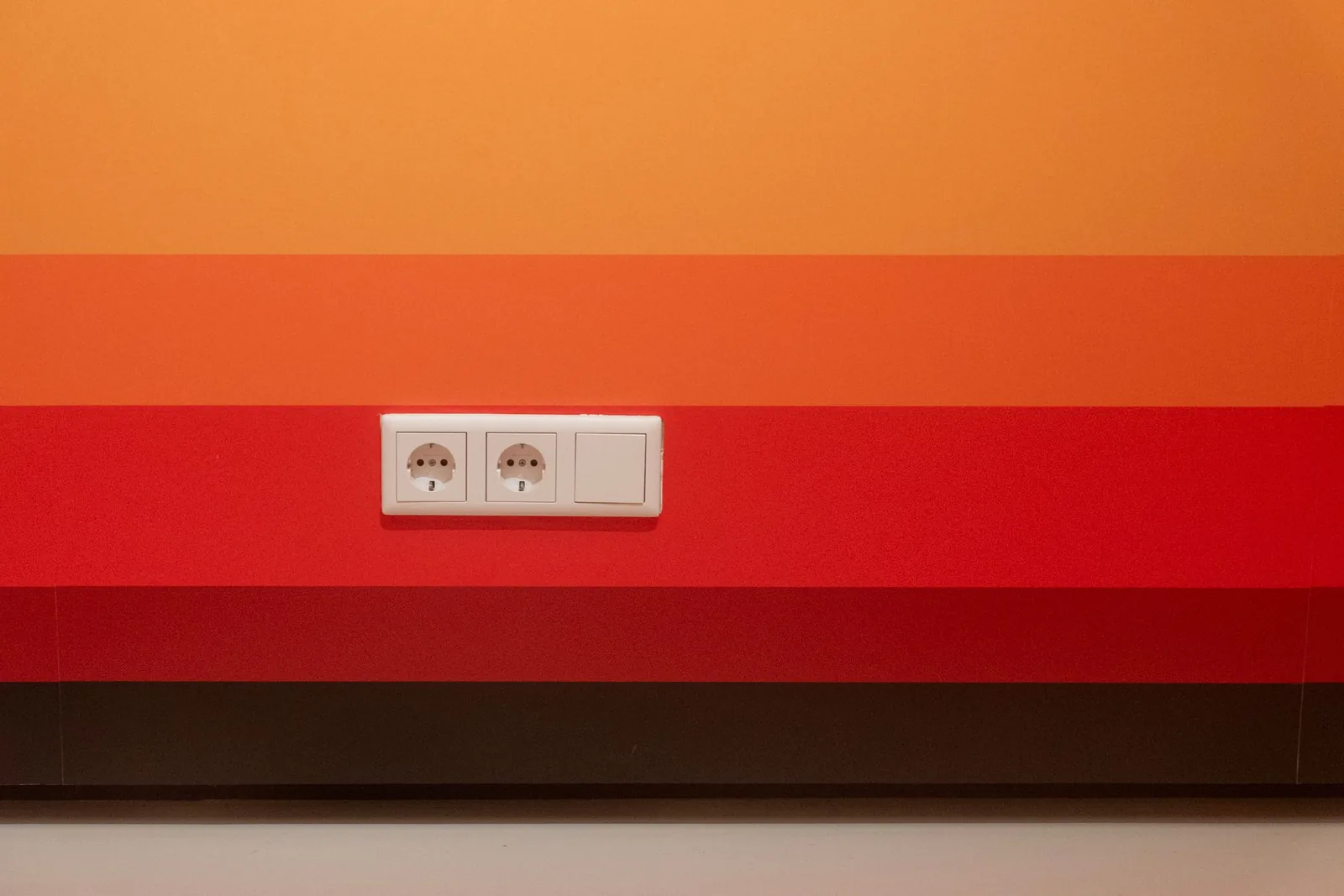 Pared con dos enchufes y un interruptor sobre franjas de pintura naranja y roja