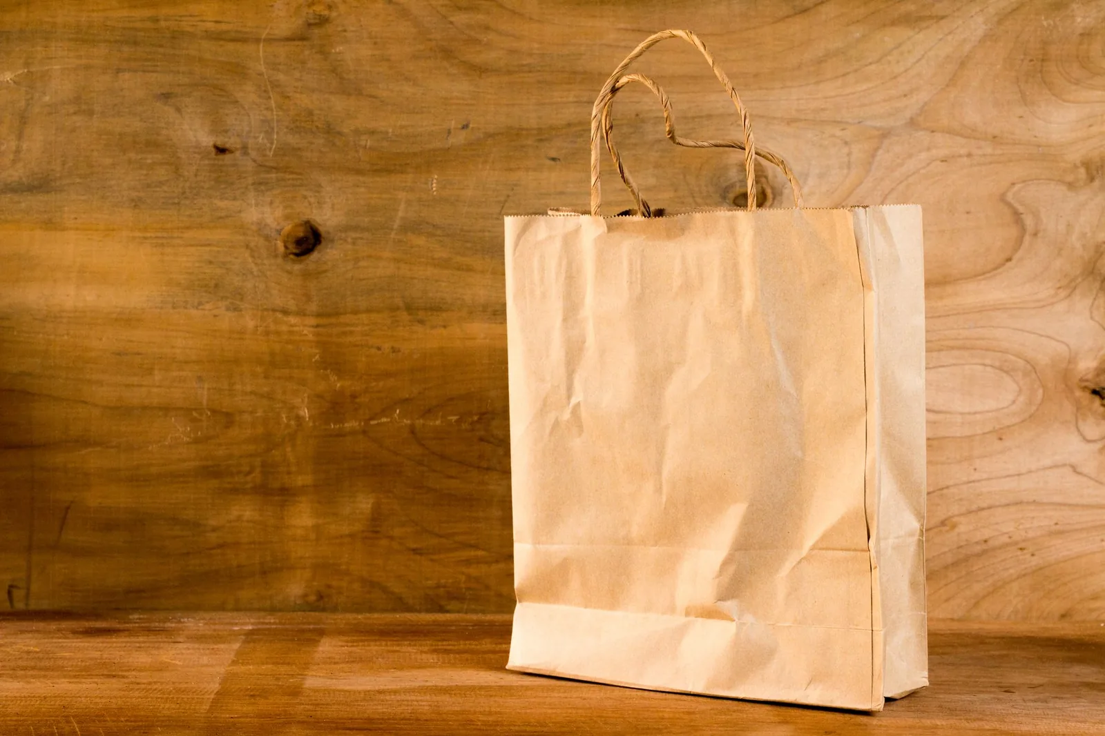 Bolsa de papel de compra lisa sobre una mesa de madera, con un fondo de tablero de madera