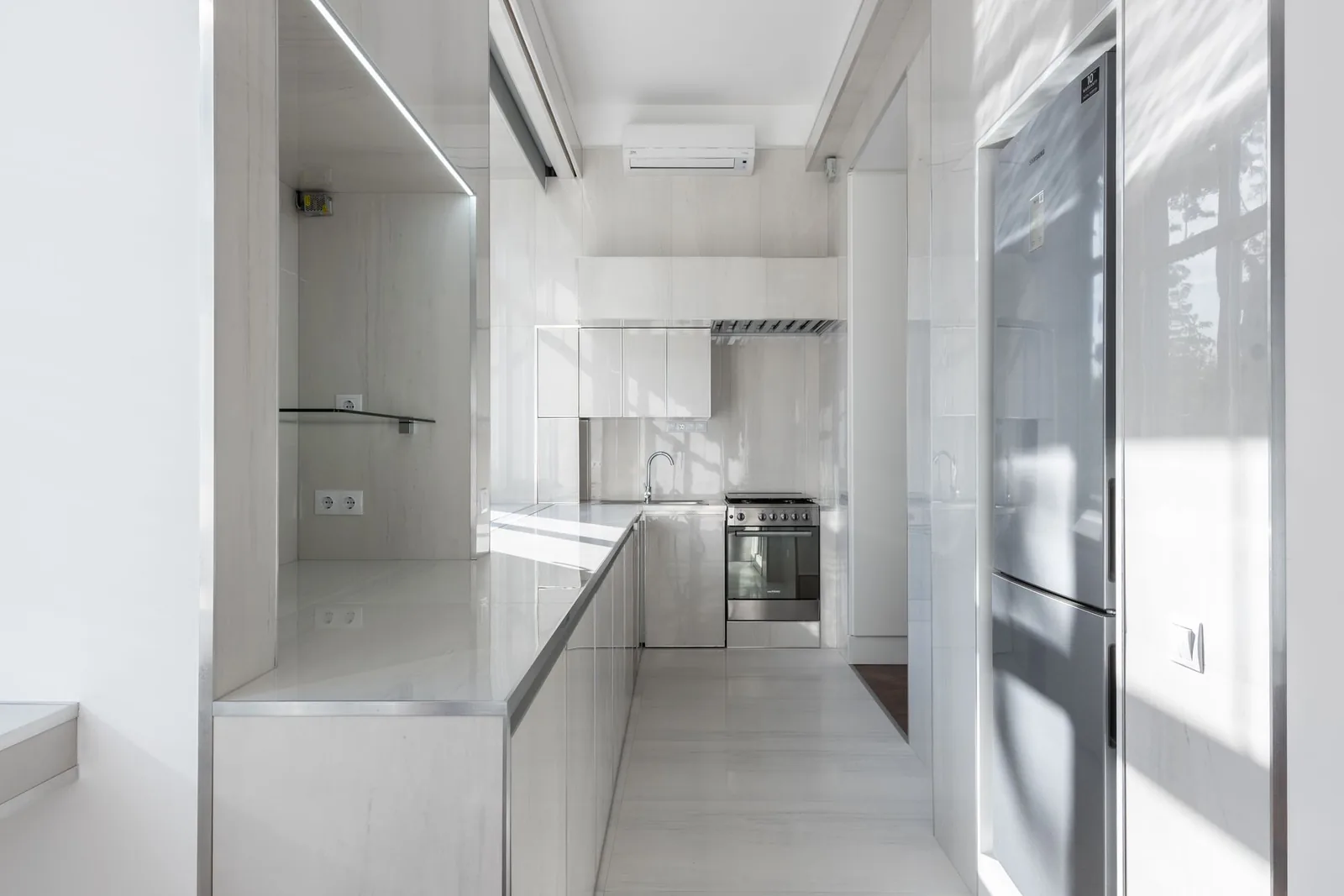 Cocina blanca luminosa con nevera de dos puertas, horno y tomas de pared de tipo europeo