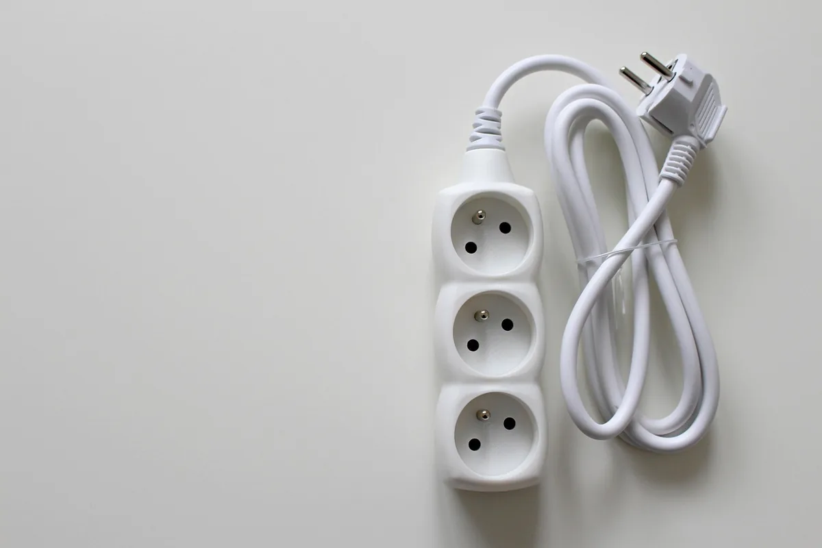 Regleta blanca de tres tomas con su cable enrollado sobre una superficie clara