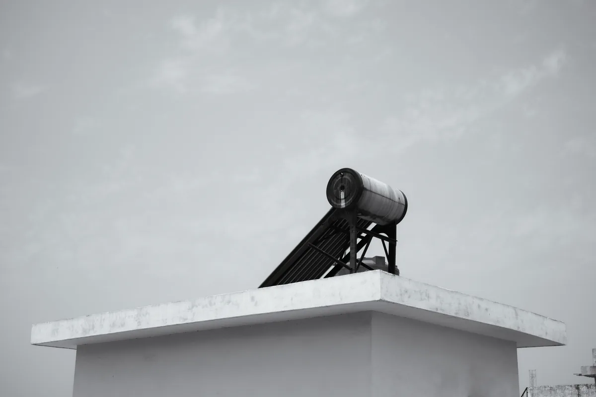 Calentador solar de agua con su depósito sobre una azotea blanca y un cielo gris