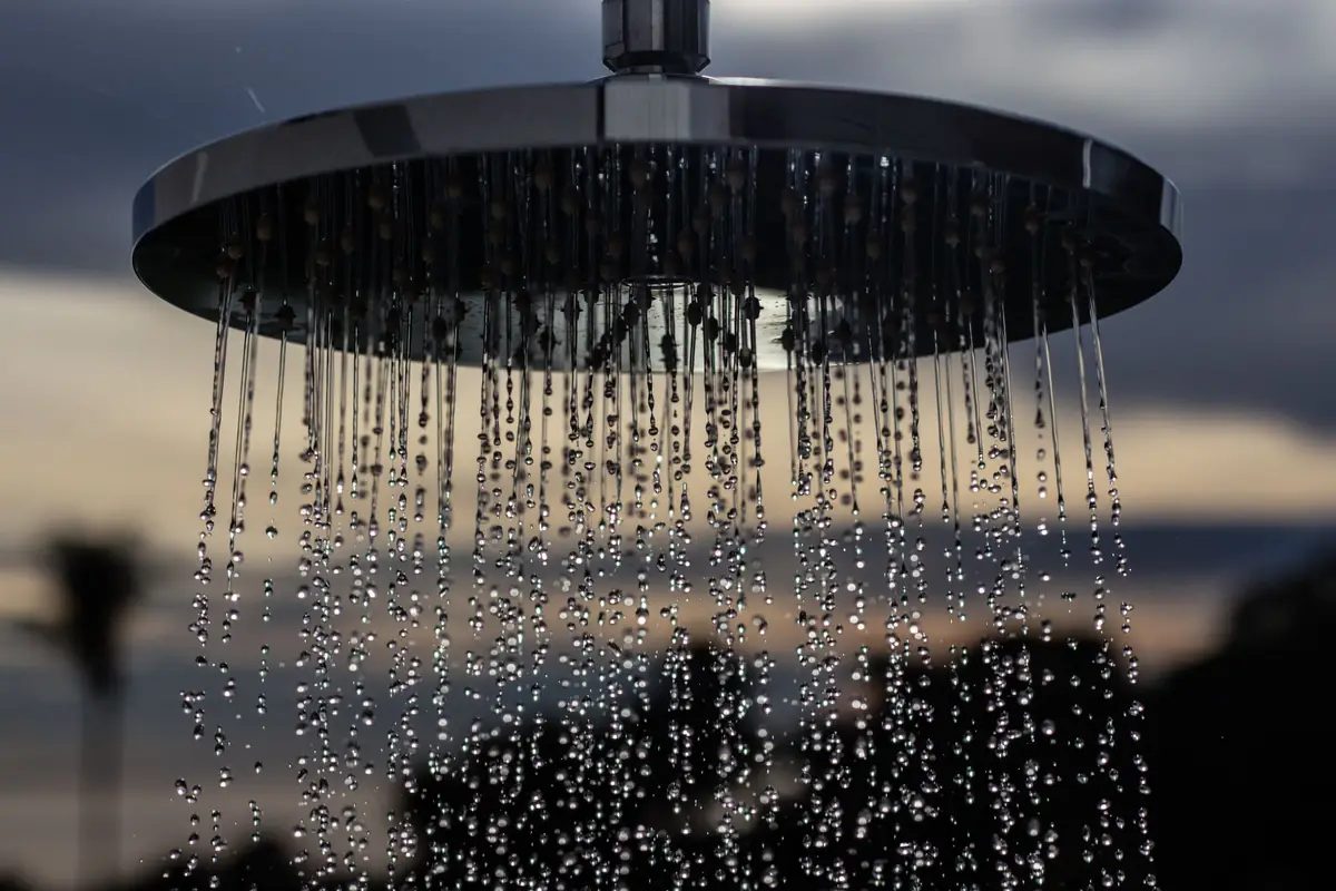 Alcachofa de ducha redonda con gotas de agua cayendo contra un cielo de atardecer